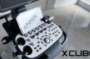ecógrafo X-CUBE 60 en vista parcial en picado con el logotipo de ALPINION reflejado en la pantalla touch y logo X-CUBE 60 a la derecha